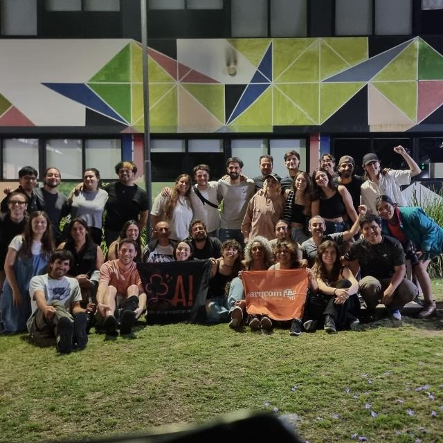 Integrantes de Agite y Arqcom, de noche frente a un edificio de la facultad, con las banderas de las dos organizaciones.
